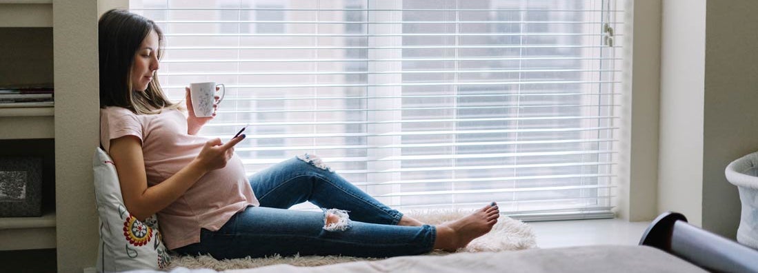 Pregnant woman using her smartphone at home. Find Health Insurance.